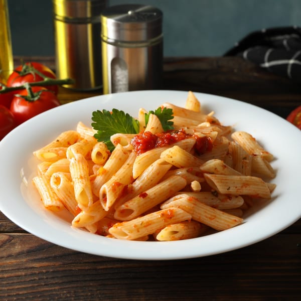 Penne pasta with red sauce and parsley in a white bowl on a wooden table.