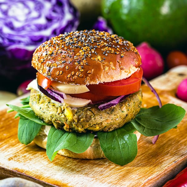 A close-up of a veggie burger with spinach, tomato, onion, and cheese on a wooden board.