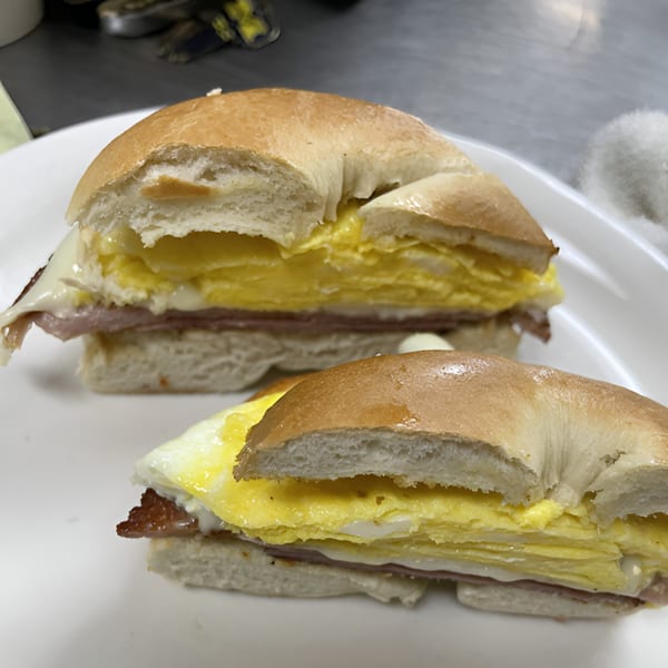 Two bagel breakfast sandwiches with egg, ham, and melted cheese on a white plate.