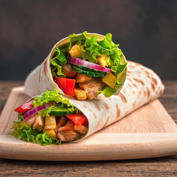 Two chicken wraps with lettuce, red onion, cucumber, and tomatoes on a wooden board.
