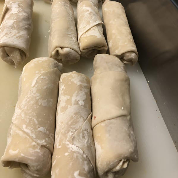Several uncooked, flour-dusted egg rolls are lined up on a white cutting board, ready for frying.