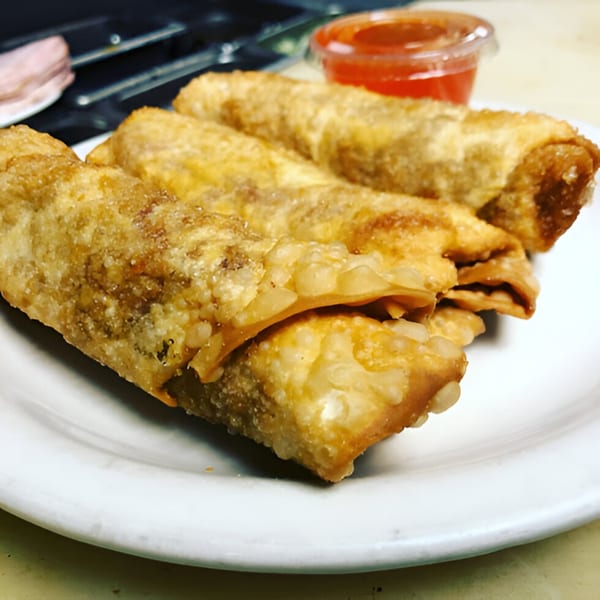 Crispy golden-brown egg rolls on a white plate with a side of red dipping sauce.