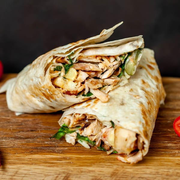 Two chicken shawarma wraps, filled with meat and vegetables, on a wooden board at Perry Street Grill.